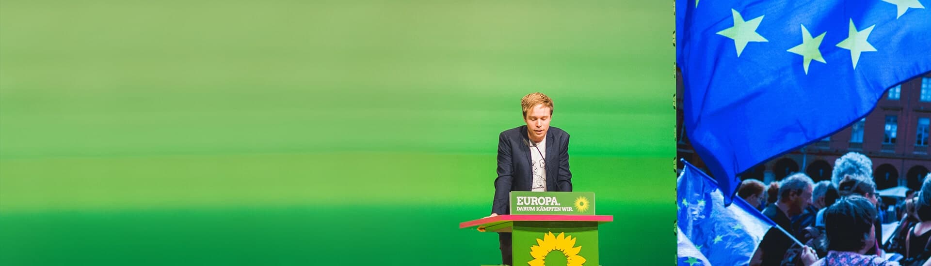 Rasmus hinter einem Rednerpult, auf dem das Logo der Grünen und der Spruch "Europa, darum kämpfen wir" zu sehen sind