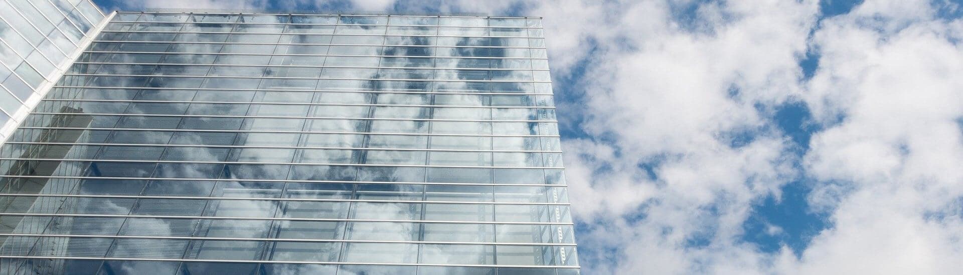 eine gläserne Hochhausfassade, schräg von unten fotografiert, die Wolken spiegeln sich darin
